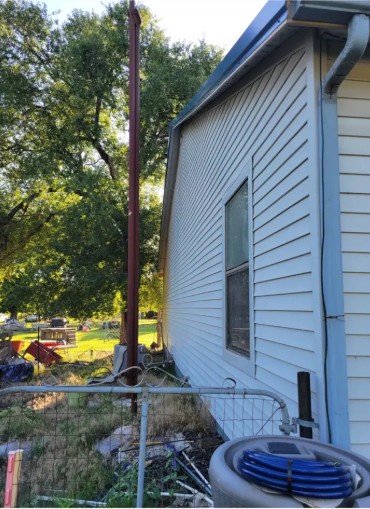 Corner of white house on small Kansas homestead showing roofline height and old antenna pole near south wall