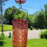 Nature's Way Petal Pink glass hummingbird feeder hanging on a porch