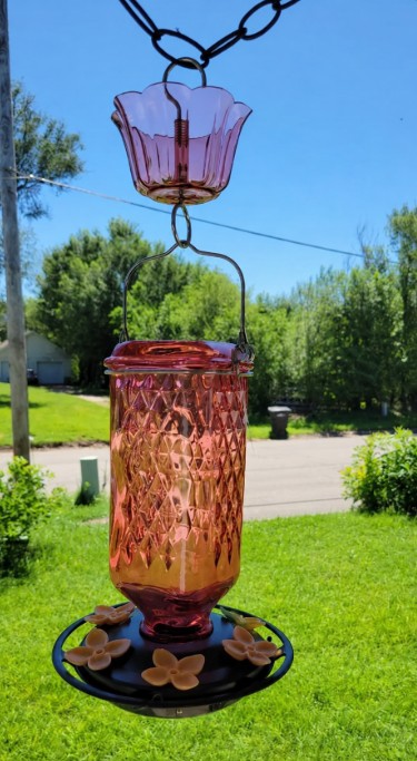 Nature's Way Petal Pink glass hummingbird feeder hanging on a porch